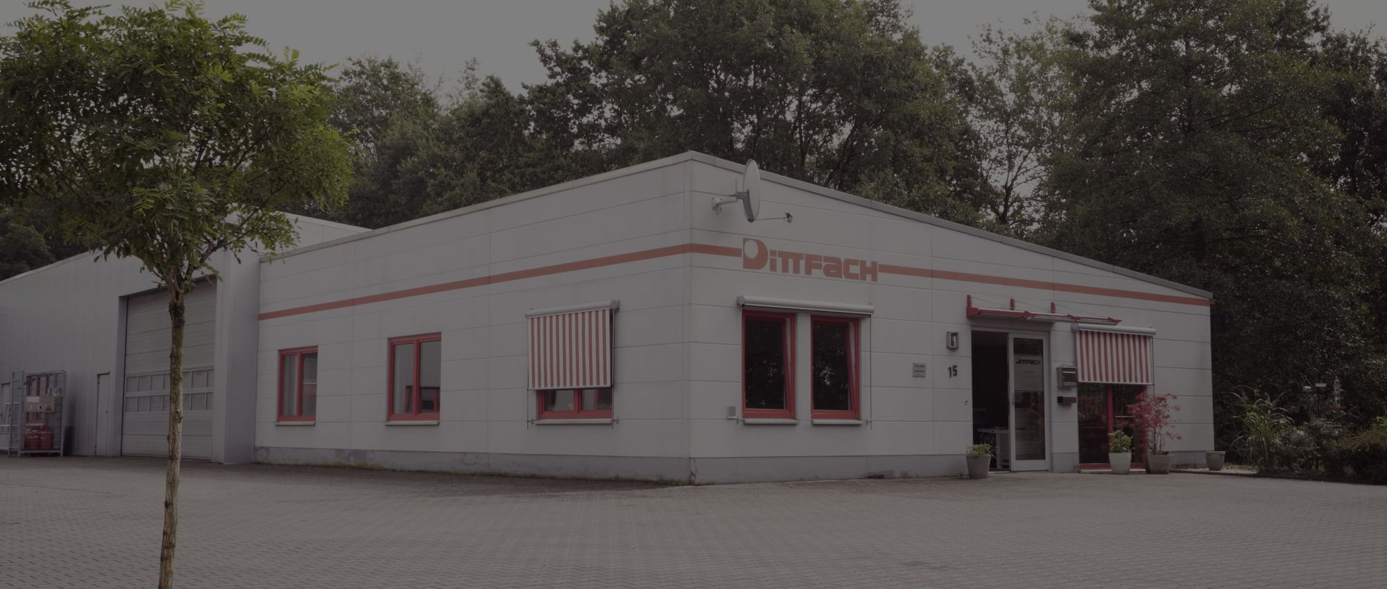 Ein modernes, helles Gebäude mit roten Akzenten und gestreiften Markisen, umgeben von Grünflächen und Parkplätzen